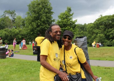 couple wearing matching yellow shirts and smiling at the camera with people standing around in lawn behind them