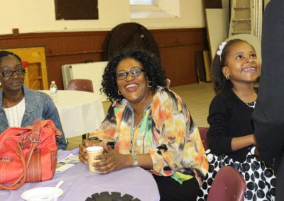 two women sitting at table and young girl smiling up at her father in the parish center